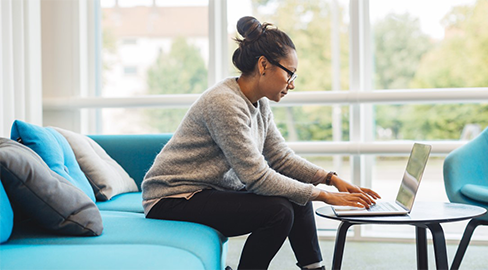 A woman at the computer sitting an a blue sofa